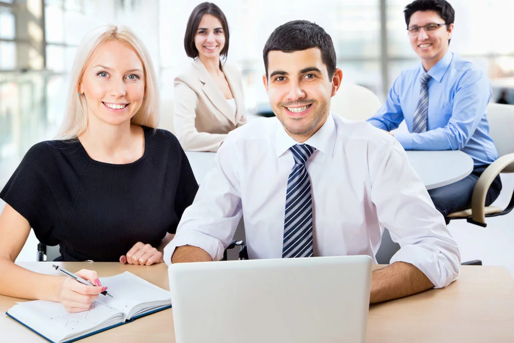Smiling business team working together at a desk with a laptop and notebook in a bright modern office