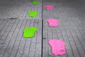 Colorful green and pink footprint stickers on pavement guiding directional movement
