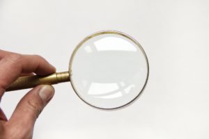 Close-up of a hand holding a magnifying glass over a white background, emphasizing focus or search.
