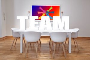 Team meeting room with large white TEAM letters on a table under colorful teamwork painting