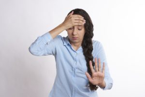 Woman holding her forehead with one hand and stopping with the other, showing stress or headache