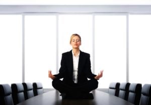 Businesswoman meditating in lotus position on a conference table, promoting workplace mindfulness and stress relief.
