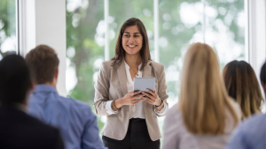 Smiling woman holding digital tablet giving presentation to attentive group in bright meeting room