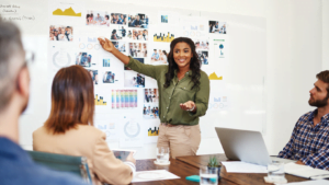 Smiling businesswoman giving presentation to team in office with charts and photos pinned on whiteboard