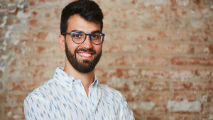 Smiling man with glasses and beard standing in front of brick wall