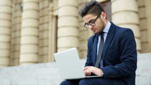 Young businessman working on laptop outdoors, mobile office and remote work training concept