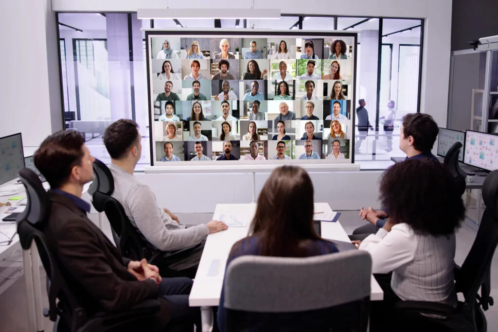Group of diverse businesspeople attending virtual meeting on large screen in modern office