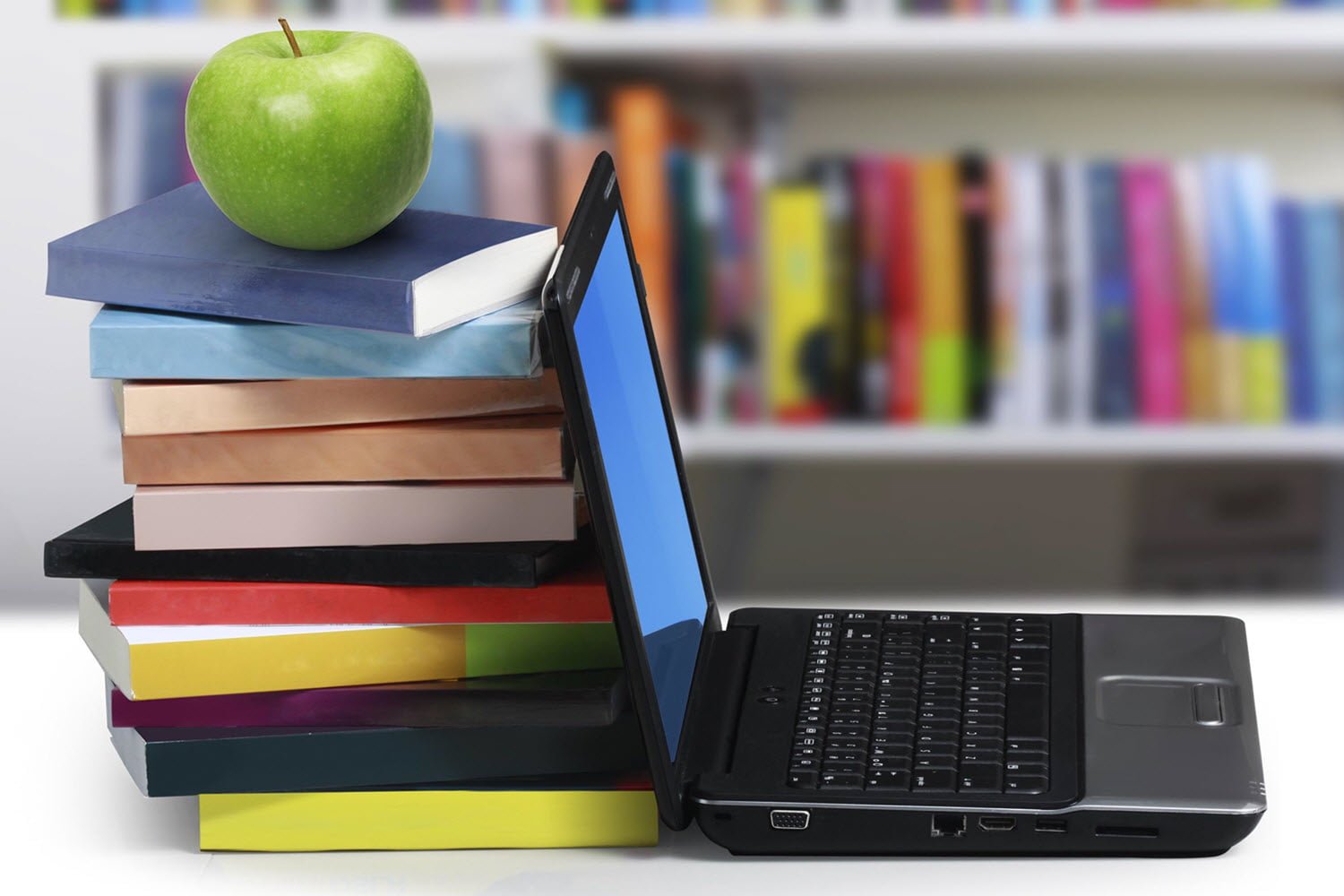 An apple on top of stacked books next to a laptop computer