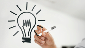 Hand drawing a light bulb symbolizing idea or creativity with black marker on whiteboard