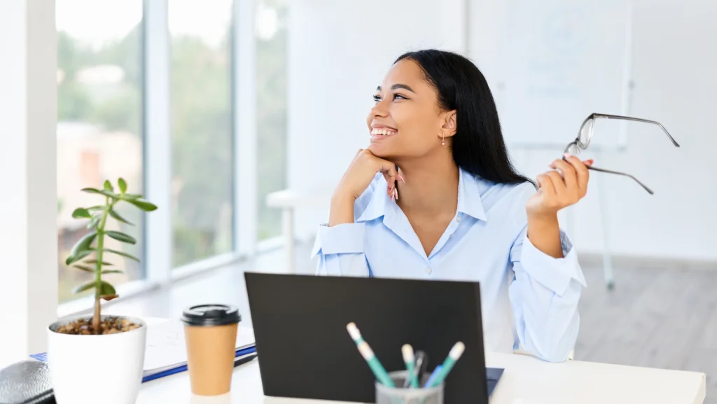 Smiling woman holding eyeglasses looking thoughtfully out office window
