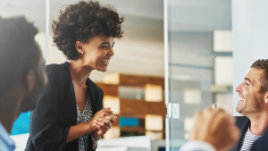 Happy young African-American businesswoman laughing and chatting with male coworkers in office meeting