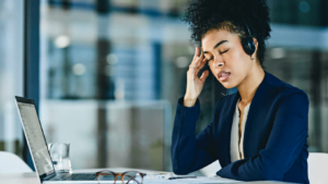 Stressed businesswoman with headset working on laptop in modern office