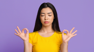Young woman meditating with eyes closed and hands in mudra gesture against purple background