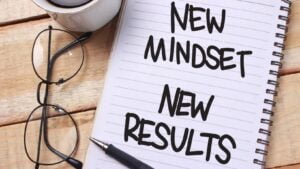 Notebook with motivational text 'New Mindset New Results' alongside glasses and pen