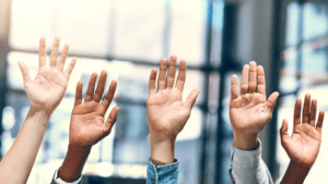 Diverse group of raised hands in an office setting representing teamwork and inclusion