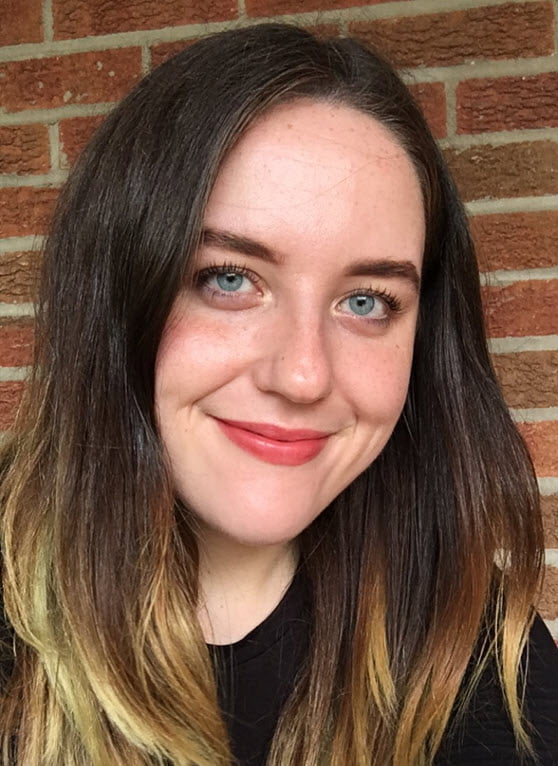 Smiling Meghan Harper with long ombre hair and blue eyes against a brick wall background