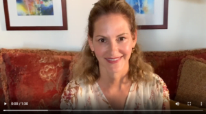 Woman smiling while sitting on a red patterned couch with framed artwork in the background