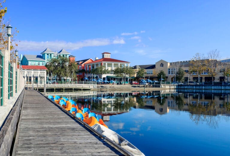 Scenic view of a waterfront boardwalk with colorful paddle boats and buildings reflecting in calm water
