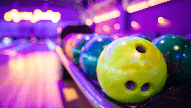 Colorful bowling balls lined up in a bowling alley with blurred background of lanes and neon lights