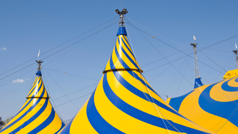 Blue and yellow striped circus tent peaks against clear blue sky