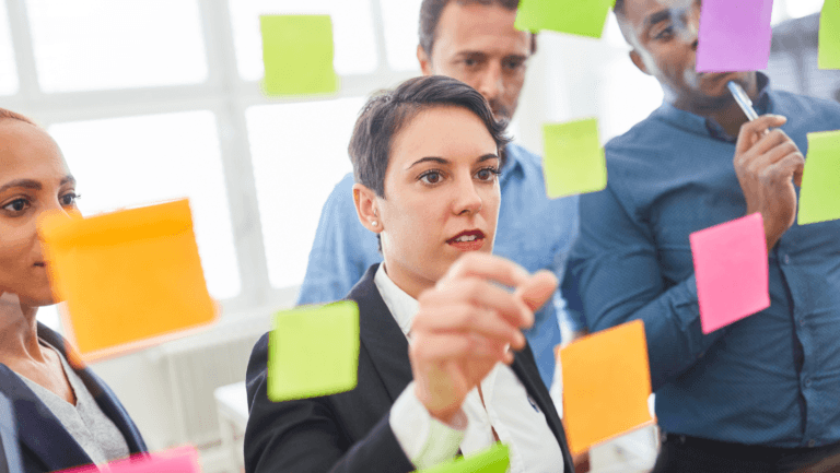 Focused businesswoman organizing colorful sticky notes on glass wall with team brainstorming