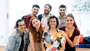 A diverse group of smiling young adults posing together indoors, showing a sense of friendship, teamwork, and positive energy in a modern setting.