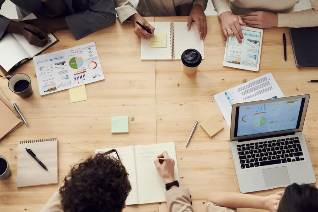 A group of diverse individuals seated at a table, each using laptops, engaged in discussion or collaboration