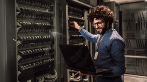 IT technician managing network cables in a server room, working with a laptop