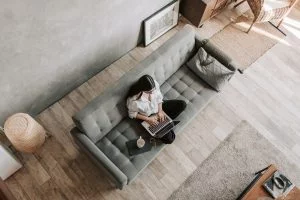 Young woman in casual denim shirt working on laptop in a bright living room from above