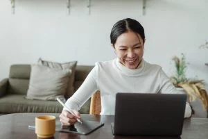 Smiling woman working on a digital tablet and laptop at home with a coffee mug nearby