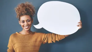 Smiling woman holding a blank speech bubble sign against a dark blue wall