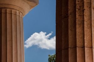 Architectural columns framing a bright blue sky with a single white cloud