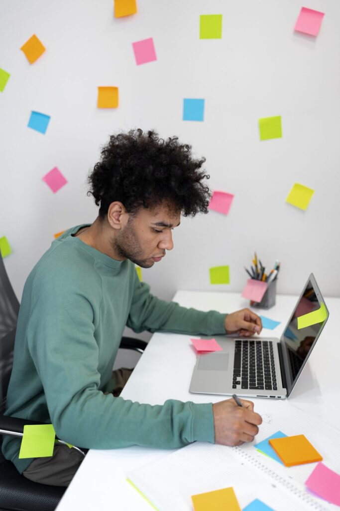 Designer sketching a session plan on paper beside a laptop, surrounded by sticky notes