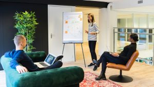 Young woman giving a presentation to colleagues in modern office with flip chart and laptops