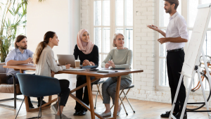 Group of multicultural professionals attending a training session with a presenter near a whiteboard