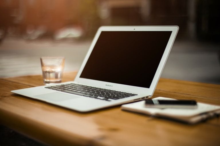 MacBook Air laptop on a wooden table with a glass of water and smartphone