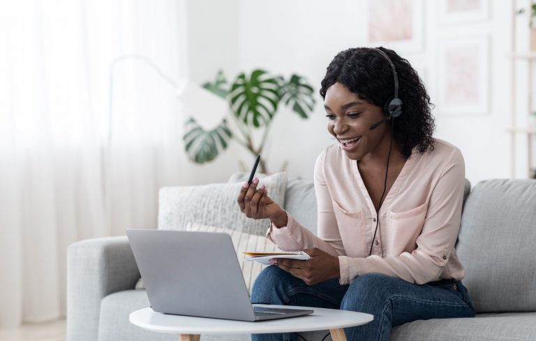 Happy woman wearing a headset talking and taking notes during an online video call at home